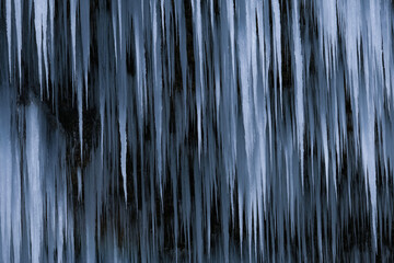 Beautiful long icicles of a frozen waterfall, with water flowing and crashing down and Ice water dripping from the tips of icicles in a cold eery and moody atmosphere in a cave in the mountains 