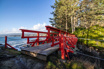 Fototapeta na wymiar A red wooden bridge between rocks on the coast of the Pacific Ocean at Point No Point in Shirley, British Columbia