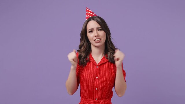 Confused puzzled brunette young woman 20s in red dress birthday hat posing isolated on violet purple background in studio. Celebrating holiday party people emotions concept. Spreading hands say oops
