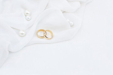 Two golden wedding rings and pearls on white background.