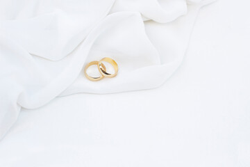 Two golden wedding rings with soft fabric on white background.
