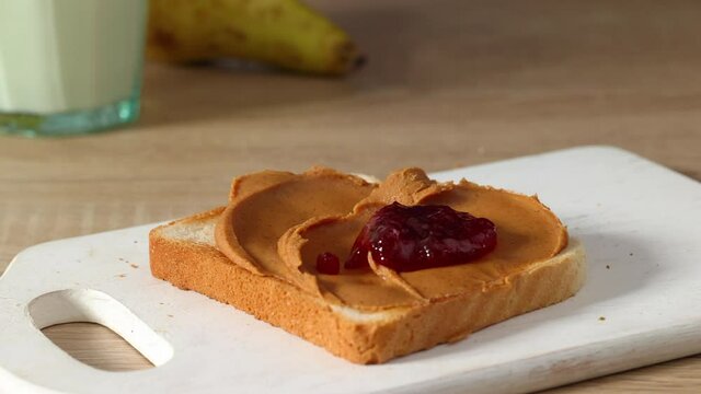 women 's hands apply jam on a slice of toasted bread with peanut butter cream close - up. home cooking breakfast