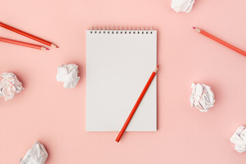 Blank white notebook with red pencils and crumpled sheets of paper on a pink background. Mockup for text.
