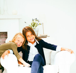two cute sisters at home playing, little girl in house interior on sofa, messing hair, fighting...