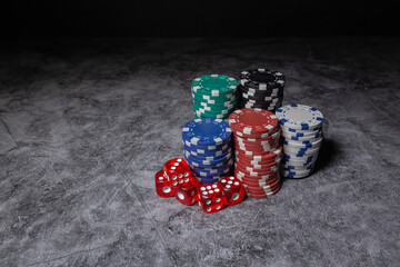 black, red, green, blue and white poker chips grouped together in towers next to some red dice leaving an empty space to the left on dark background