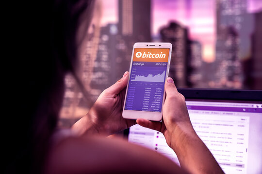ROSARIO, ARGENTINA - FEBRUARY 19, 2021: Bitcoin chart in a screen of mobile phone. Business woman with smartphone in her hands. Virtual money investment. Cryptocurrency exchange concept.