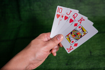 Male hand holding Poker playing Cards over a green Texture wooden table
