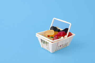 sweet and tasty candy - marmalade, jelly candies, in the toy food basket, shopping trolley on a blue background with space for text. 