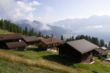Fünf Holzhäuser auf dem Berg in der Schweiz. Im Hintergrund ist Nebel, Bäume, Landschaft und Wolken. Urlaub in der Schweiz.