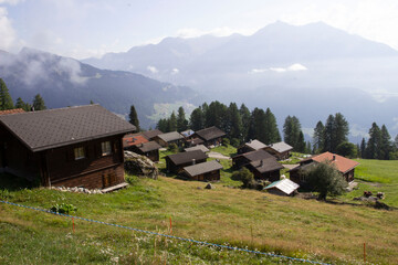 Mehrere Holzhäuser auf dem Berg in der Schweiz. Im Hintergrund ist Nebel, Bäume, Landschaft und Wolken. Urlaub in der Schweiz.