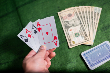 Male hand of compulsive gambler holding Poker Cards over a green Texture wooden table, gambling with some american dollars 