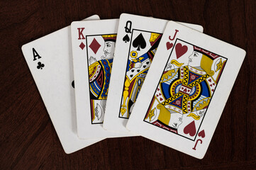 Ace of clubs, king of diamonds, queen of spades, and jack of hearts playing cards on wood table