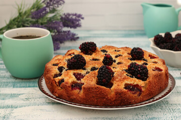 Homemade pie with blackberries and coconut chips on a light blue background. Closeup
