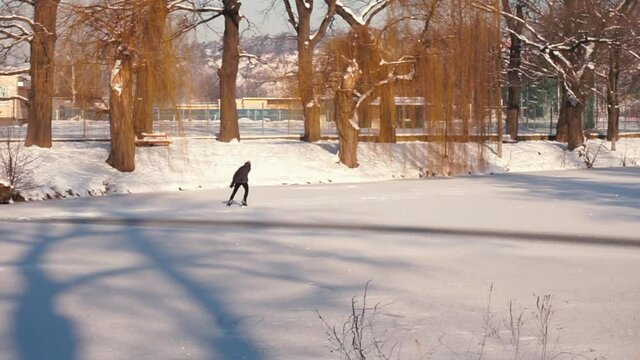 A lonely man skates on the ice of a lake in a city park. He spends his leisure time in self-isolation. Sport life.