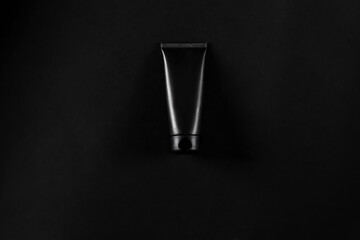 Black cream tube on black table. Mockup directly above lowkey flat lay.