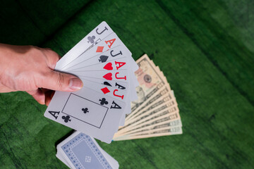 Male hand of compulsive gambler holding Poker Cards over a green Texture wooden table, gambling with some american dollars 