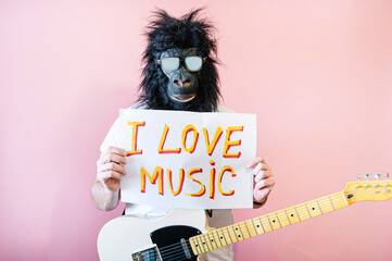 Man with gorilla mask and hanging electric guitar showing a sign that says I love music