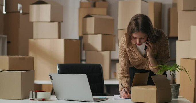 female worker of small delivery company is accepting order by cellphone, writing notes in notebook
