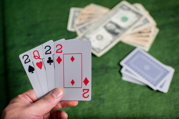 Male hand of compulsive gambler holding Poker Cards over a green Texture wooden table, gambling with some american dollars 