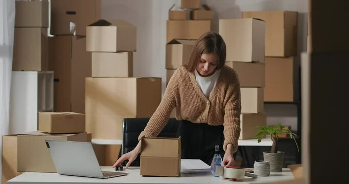 female worker of warehouse is packaging order and supporting documents in cardboard box in room of apartment, small business and entrepreneurship