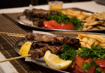 .Fried souvlaki, traditional lamp kebab with fresh salad and sauce in plate on wicker surface.