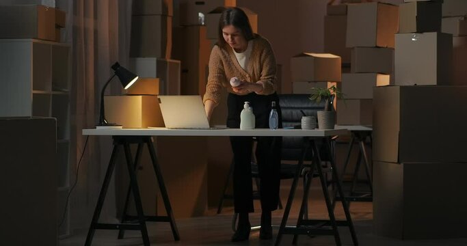 businesswoman is working alone in her home warehouse with cosmetic and household chemicals at night, learning products