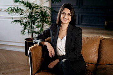 Psychologist Portrait of a business woman brunette. Employee lawyer break during work. Business stylish black suit. Copy space. Relaxing on the sofa in a modern office.