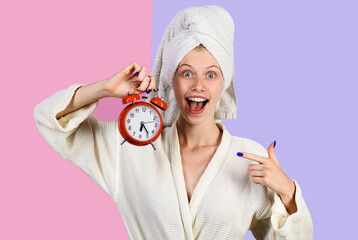 Smiling morning woman with alarm clock. Happy girl in bathrobe with alarm watch. Woman pointing on...