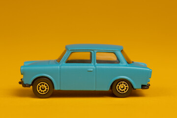 Teal colored miniature car isolated with sharp shadow underneath. Studio still life old fashion toy against a seamless yellow background.