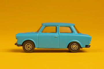 Small teal colored miniature Lada type car isolated with sharp shadow underneath. Studio still life old fashion toy against a seamless yellow background.