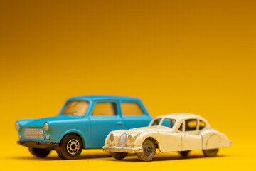 Sideview of a couple of oldtimer vintage miniature cars on clean colorful background. Studio toy still life against a seamless yellow background.