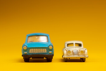 Front view of two vintage old timer authentic miniature cars against a seamless yellow background. Studio colorful toy still life.