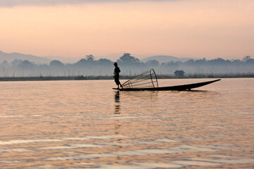Intha leg-rowing fisherman with basket net near floating gardens on Inle Lake at sunrise, Myanmar (Burma)