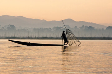 Intha leg-rowing fisherman with basket net near floating gardens on Inle Lake at sunrise, Myanmar (Burma)