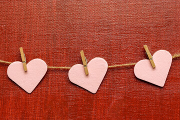 A strand of three pink hearts attached to twine by mini clothes pins hanging across a red painted canvas. Concepts: Love, Valentine, Kindness, Friendship