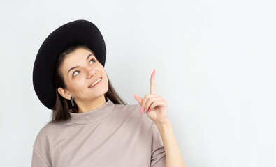 Portrait of a smiling young woman pointing and looking up on brown t-shirt against white background...