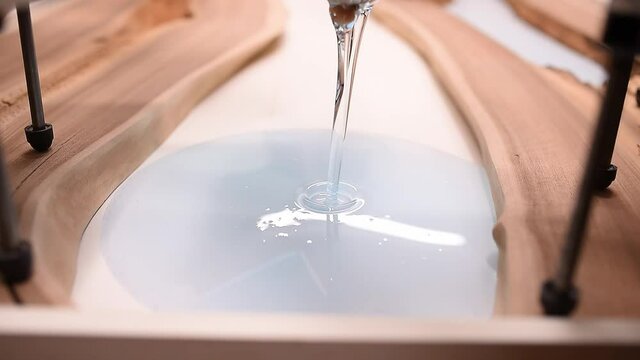 Process making of a craft resin and wood table. Liquid epoxy is poured into a mold with wooden blanks.