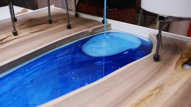 Process making of a craft resin and wood table. Liquid epoxy is poured into a mold with wooden blanks.