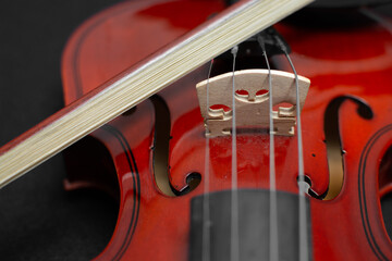 Close view of a classical small violin, strings and bridge over a dark black blanket background

