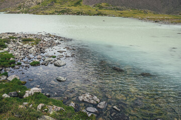 View from top to turquoise mountain lake with transparent water. Atmospheric mountain landscape with turquoise water surface of glacier lake among stones and grass. View from above to highland lake.