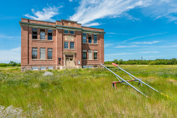 The old, abandoned Aneroid Consolidated School in Aneroid, Saskatchewan, Canada with teeter totters in the foreground