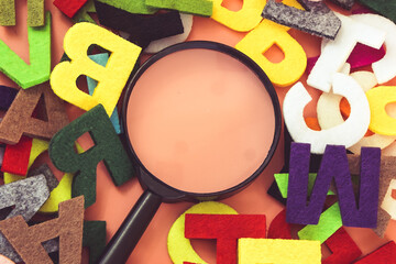 Magnifying glass with colorful alphabet on pink  background. Education concept.
