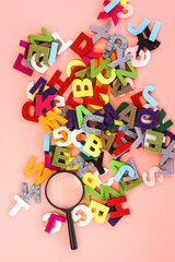 Magnifying glass with colorful alphabet on pink  background. Education concept.
