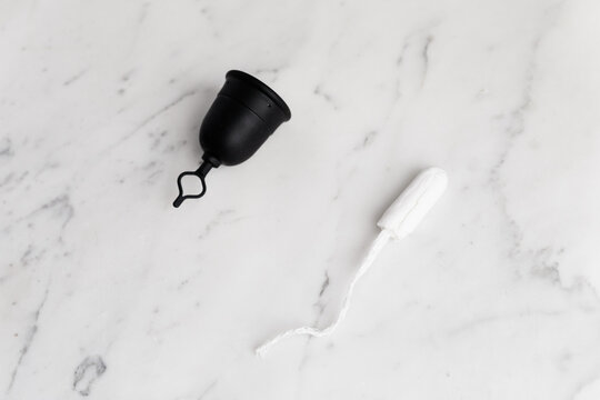 Reusable and sustainable menstrual cup next to tampon on marble