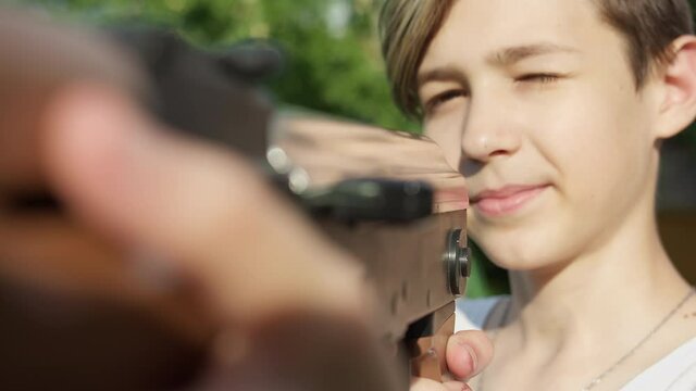 portrait of smiling boy reloading a kalashnikov assault rifle outdoors, boy playing with toy guns, children's games