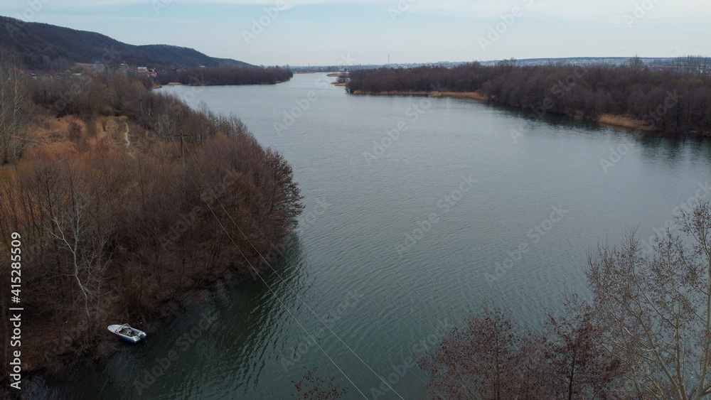 Sticker Aerial shot of a beautiful lake with buildings and dense trees in the background of blue sky