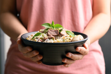 Rice noodle soup with pork, pork ball and vegetables in a bowl holding by woman hand, Thai noodles soup