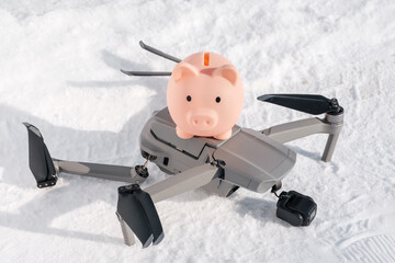 Broken gimbal camera and drone motor arm after crash and piggy bank on snow in winter outdoor closeup. Expensive repairs concept