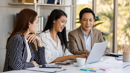 group of Asian businesspeople working communicating and looking at laptop screen while sitting on a desk together. Concentration brainstorming with good teamwork