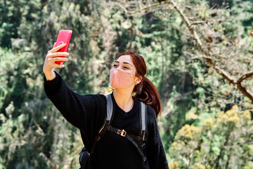 portrait of young woman with red hair and protective mask taking selfies with cell phone in the...